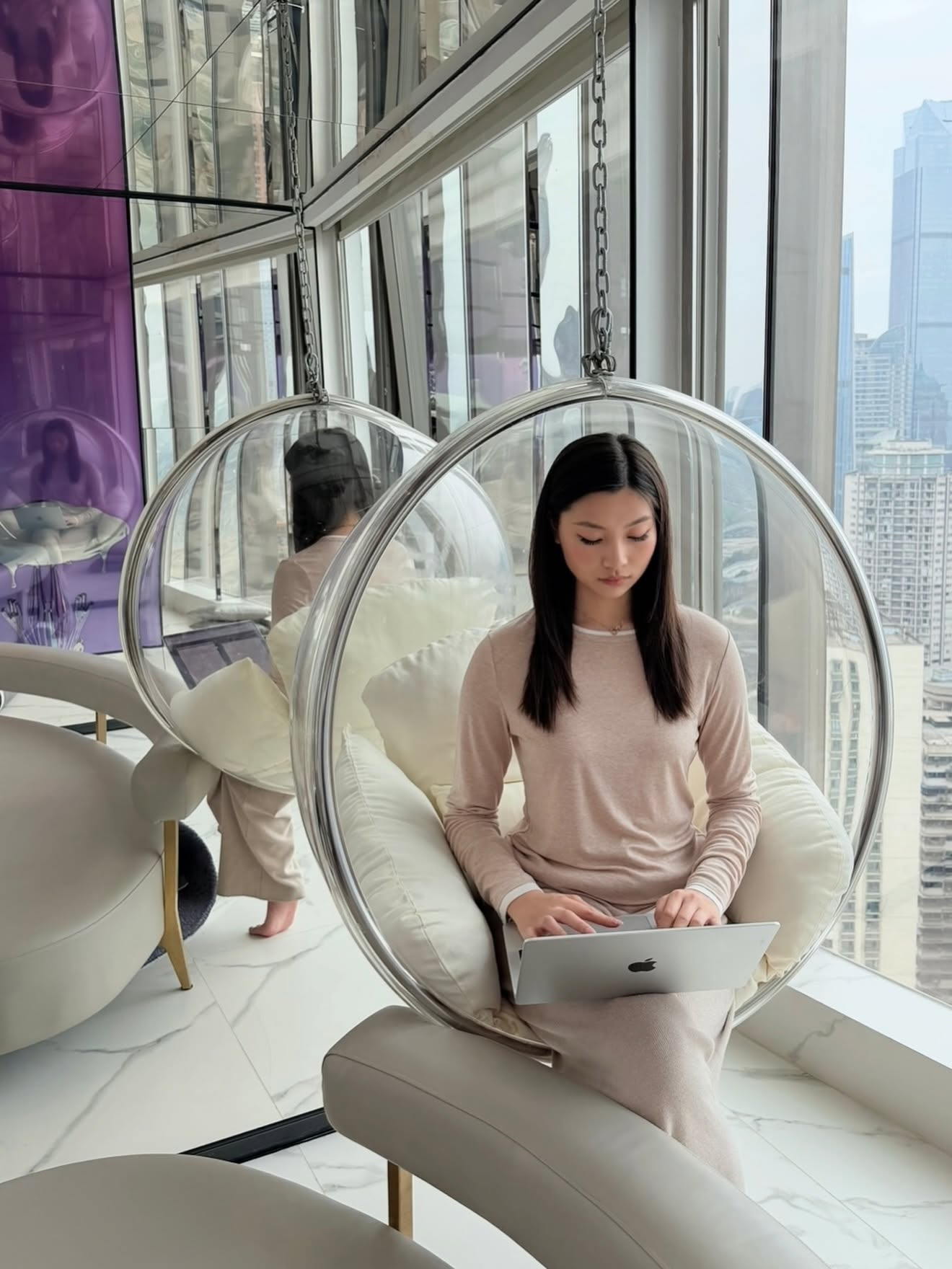 Mia Yilin working on a laptop in a bubble chair by the window