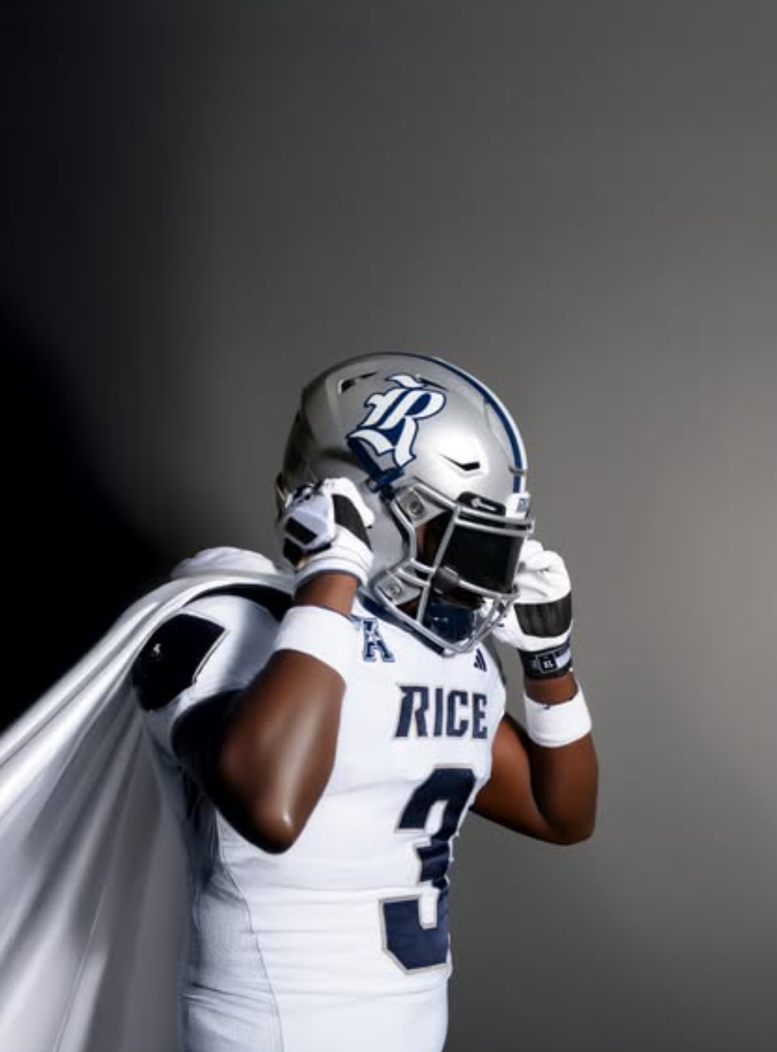 Quincy Tchikou in a studio pose adjusting his helmet with a cape draped over his shoulder