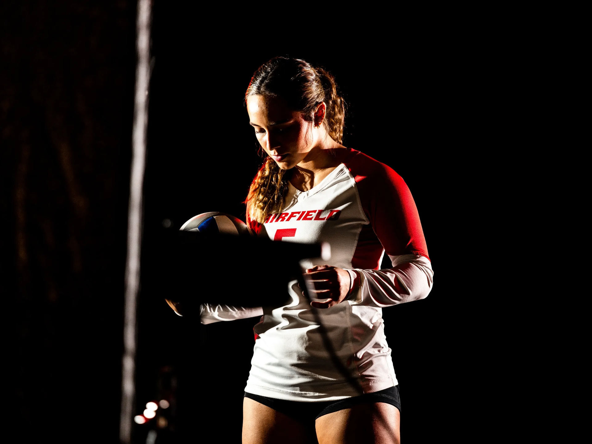 Delaney Moon in a Fairfield jersey holding a volleyball under dramatic spotlight