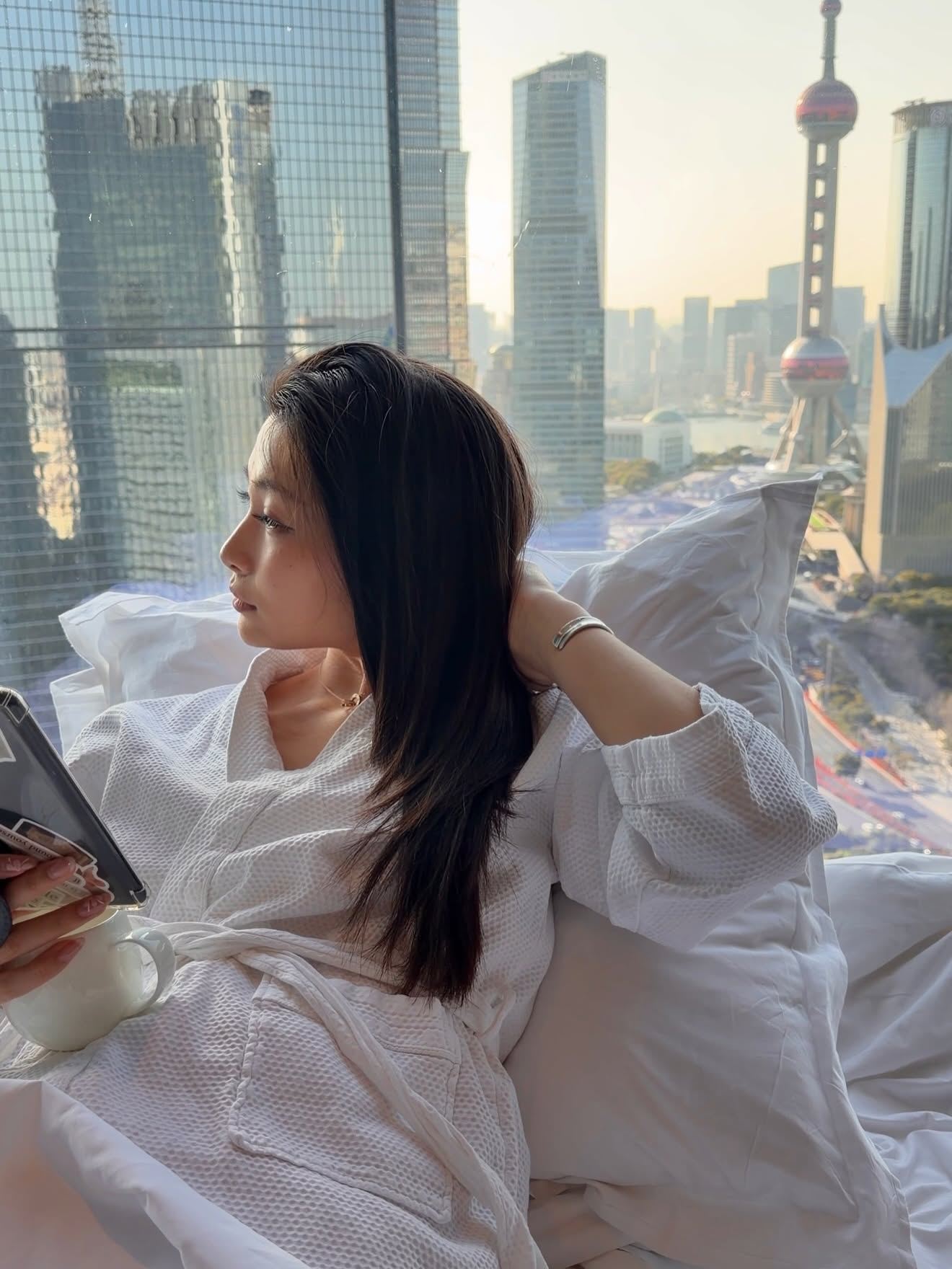 Mia Yilin in a robe by a city skyline window