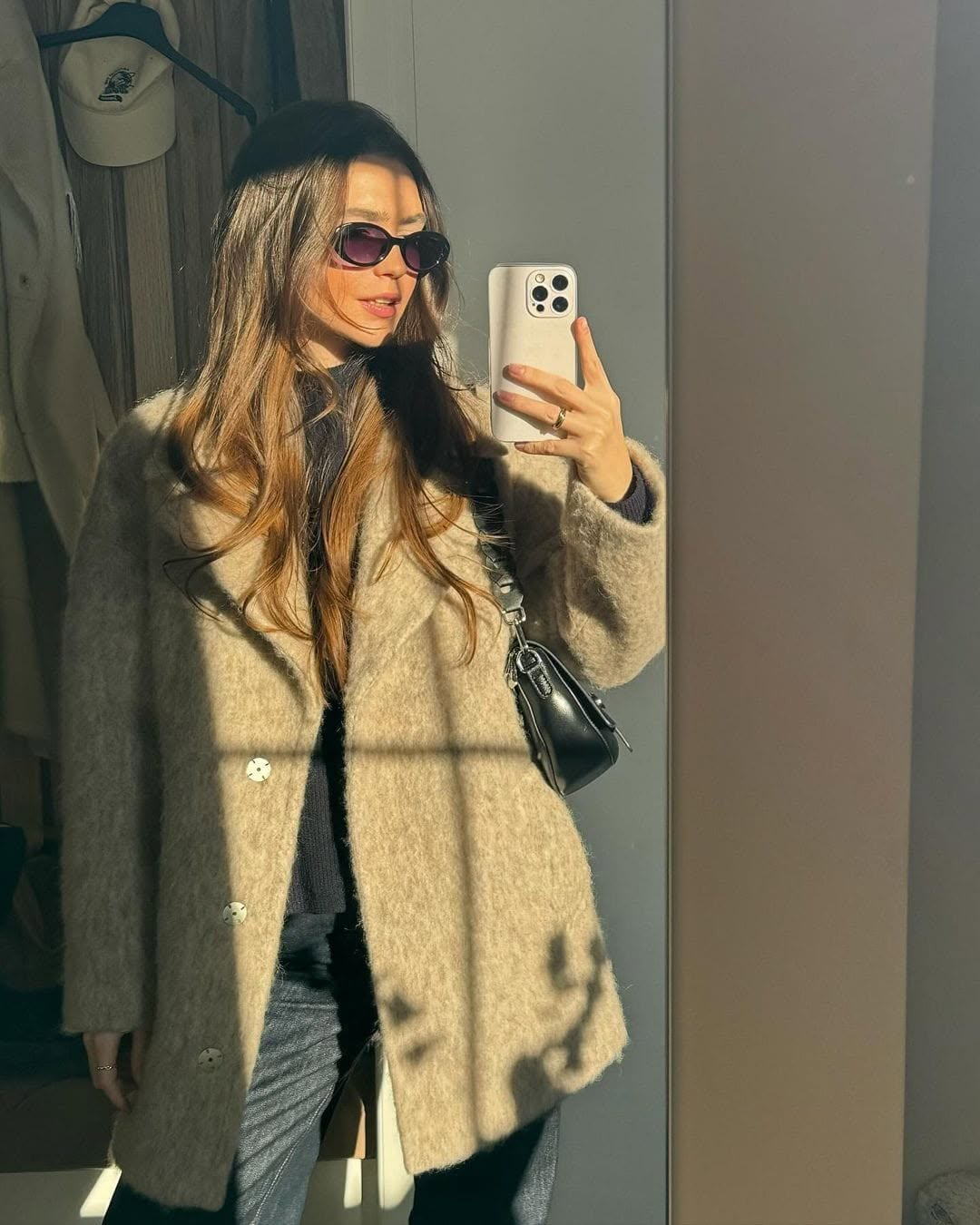 Tetiana Soviak in a beige coat and sunglasses mirror selfie