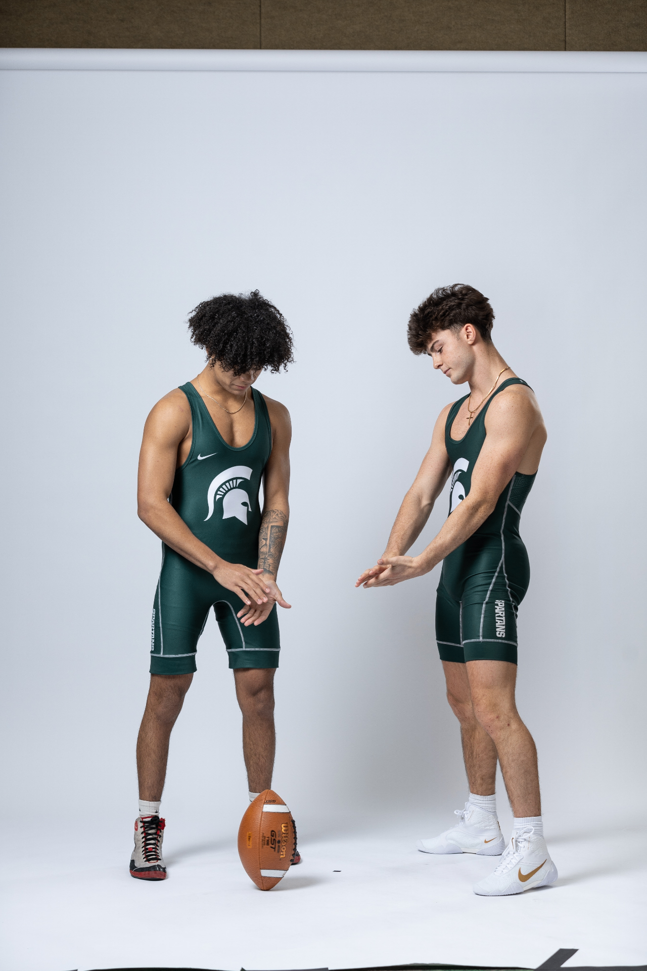Sammy Agnello posing in studio with another Michigan State athlete and a football