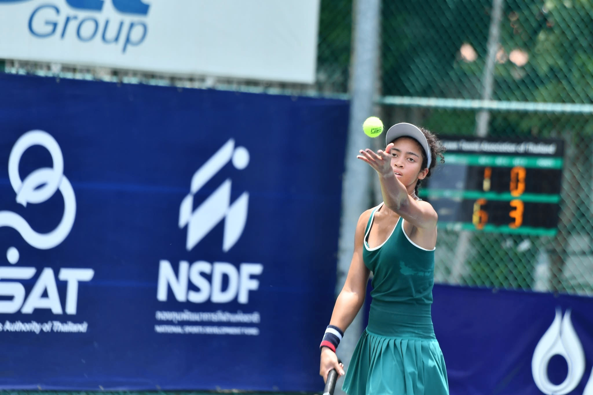 Leilani Hereford tossing the ball for a serve in a green dress at a tournament in Thailand