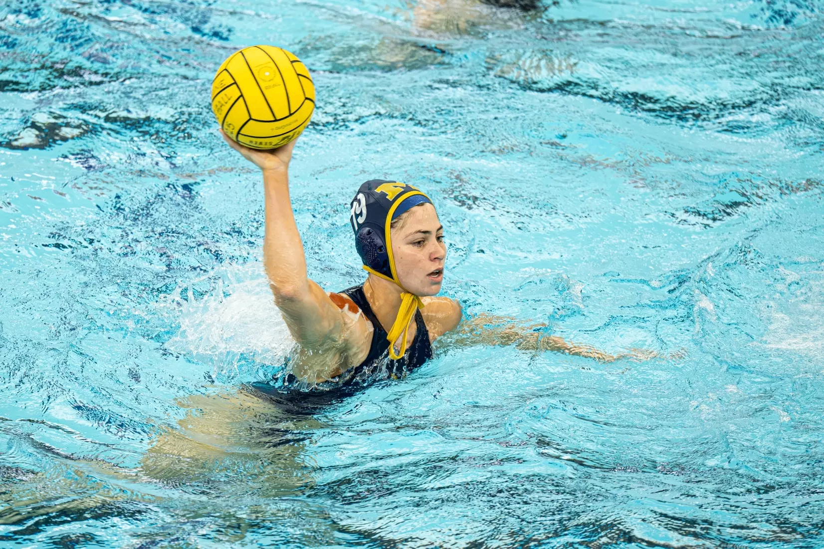 Sophia Panossian shooting a yellow water polo ball in a Michigan cap