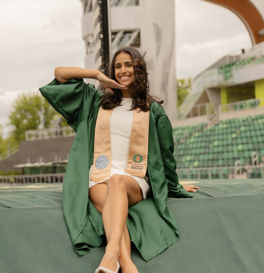 Bella Nilsen seated at Hayward Field in University of Oregon graduation regalia