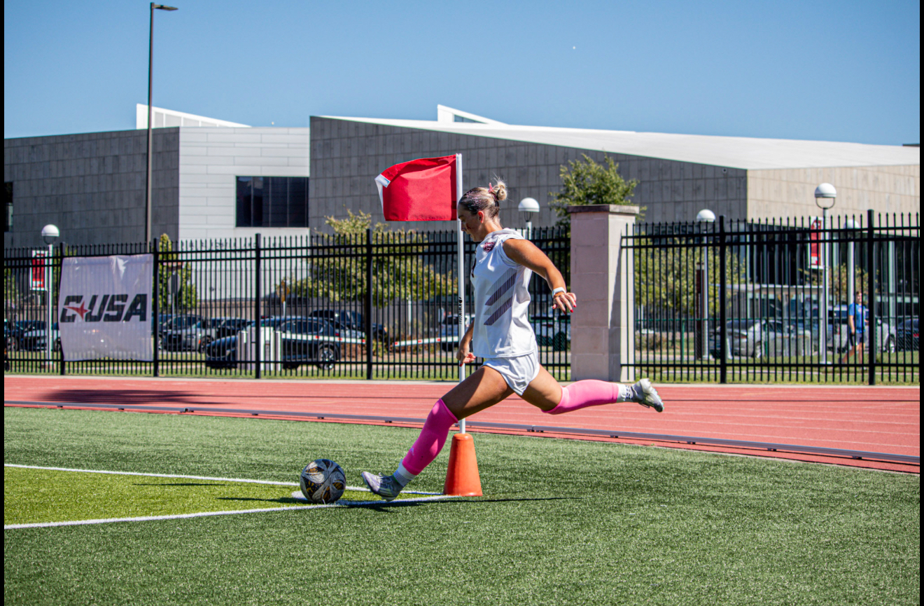 Macee McKenna in pink socks sprinting toward the corner flag in Missouri State whites
