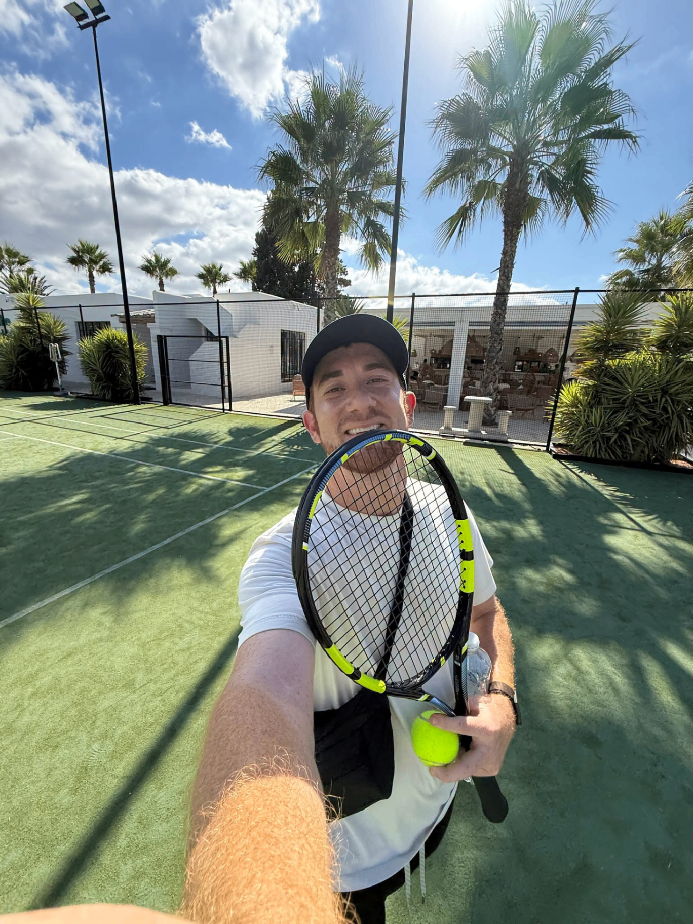 Drew Binsky on a tennis court with palm trees behind him
